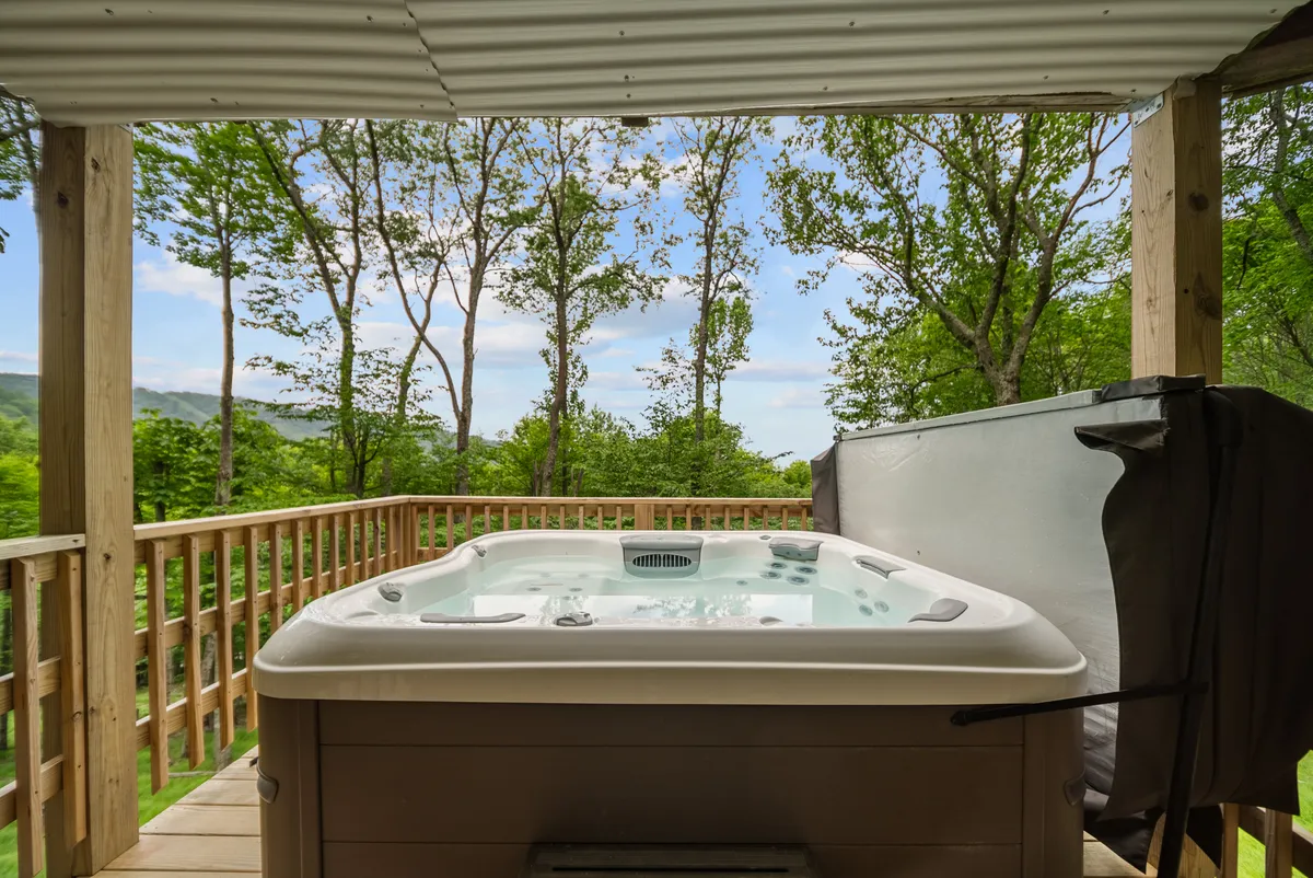 An exterior scene showing a private hot tub on a wooden deck, surrounded by lush trees and a sturdy deck railing. The tranquil space invites relaxation with mountain breezes, and the view hints at the endless vistas beyond. The hot tub is ideally positioned for stargazing or soaking after a day of adventure.