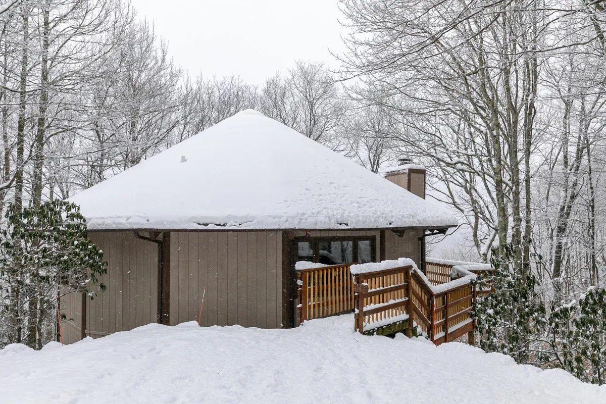 A striking winter exterior of Vista 360 featuring a snow-covered roof, rustic wooden railing, and tranquil surrounding trees. Footprints in the snow hint at recent outdoor adventures, while the inviting structure promises warmth inside.