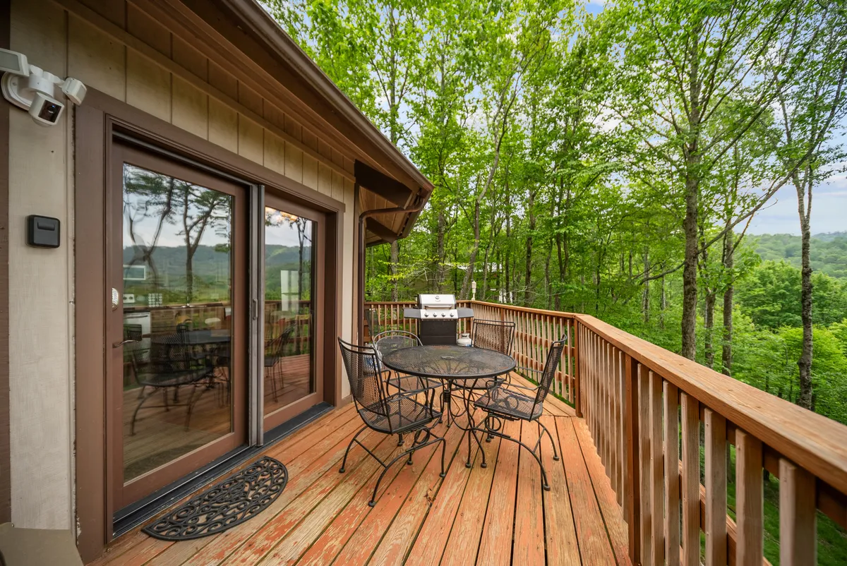 This image shows an outdoor dining set and grill on a deck surrounded by trees, evoking the atmosphere of shared meals or barbecues in nature. The setting is serene and inviting, encouraging both group activities and intimate gatherings.
