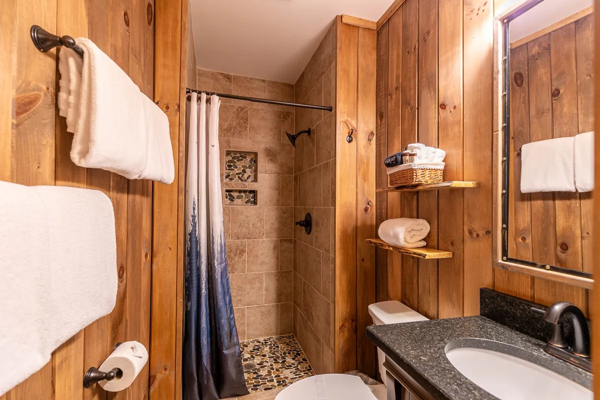 A bathroom with wooden walls, a modern shower area, and a sink with a mirror. Natural light and wood elements give the space a spa-like, calming vibe—perfect for refreshing after a day outdoors.